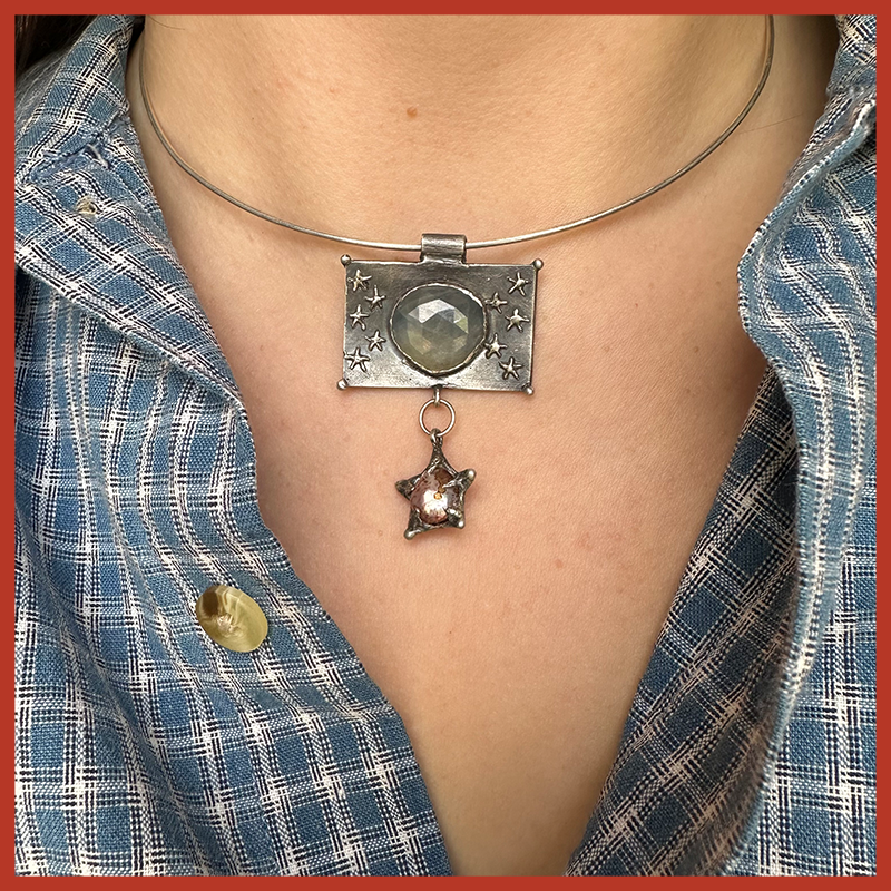 Silver choker necklace with a sapphire and pearl worn by someone in a checkered shirt.