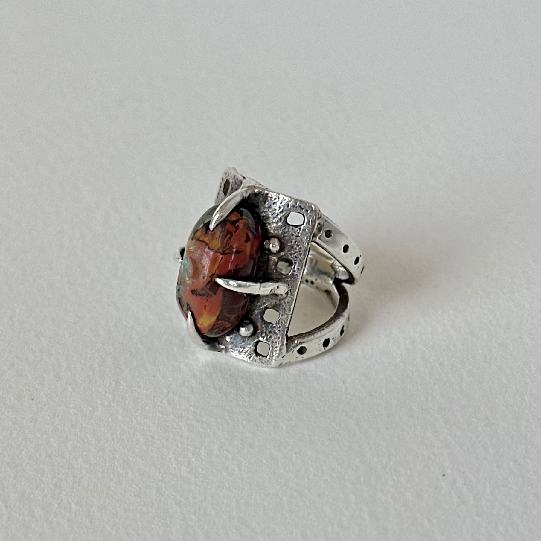 Boulder opal prong set on silver ring with textured background and split shank design.