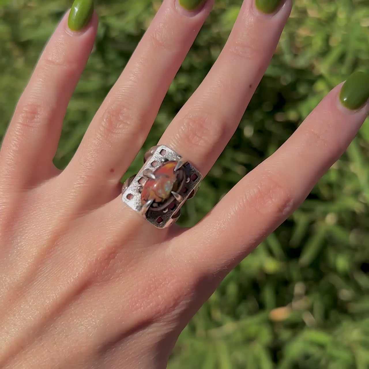 Short video of a hand modeling a silver ring with a prong set boulder opal and square cutout design.