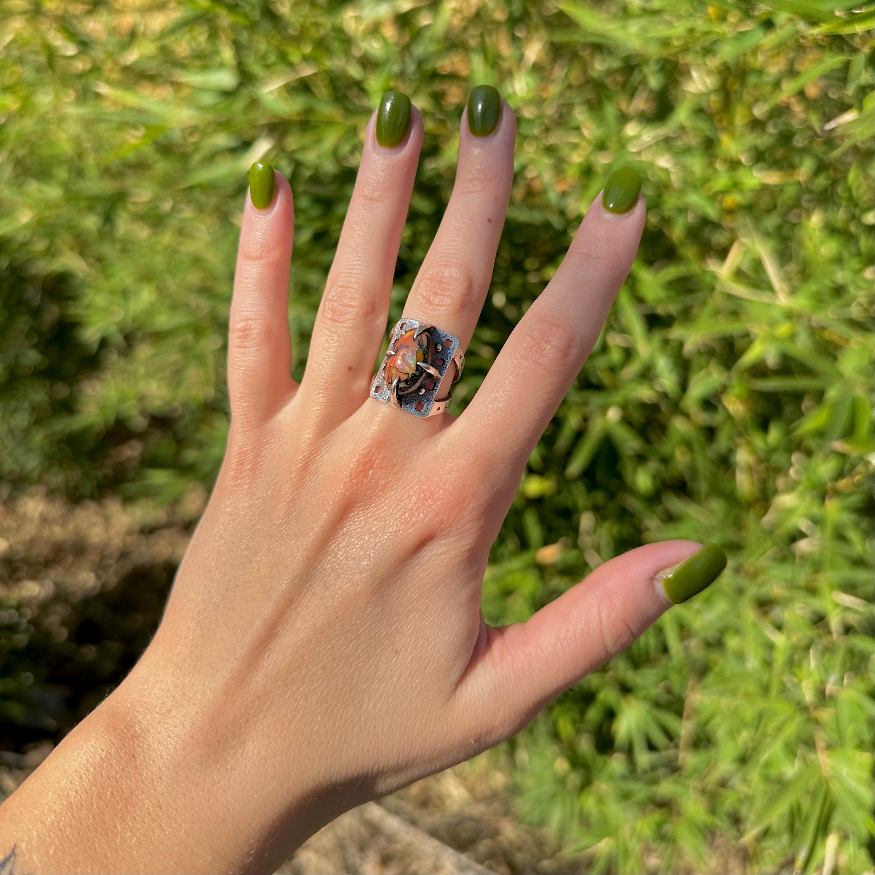 Hand modeling silver ring designed by Martha Sudderth with a prong set boulder opal and square cutout details.