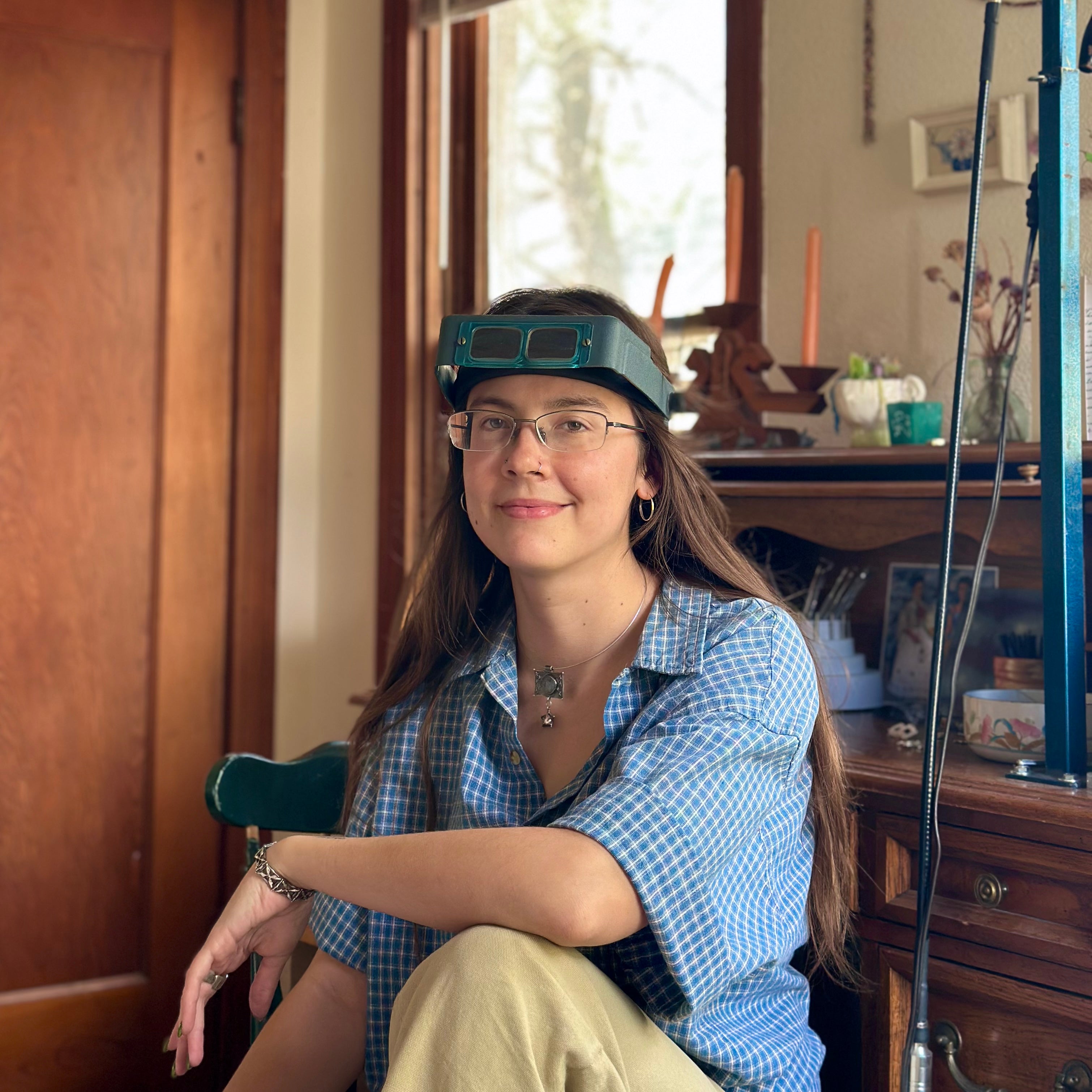 Independent jeweler Martha Sudderth sitting at her workbench wearing optivisors.